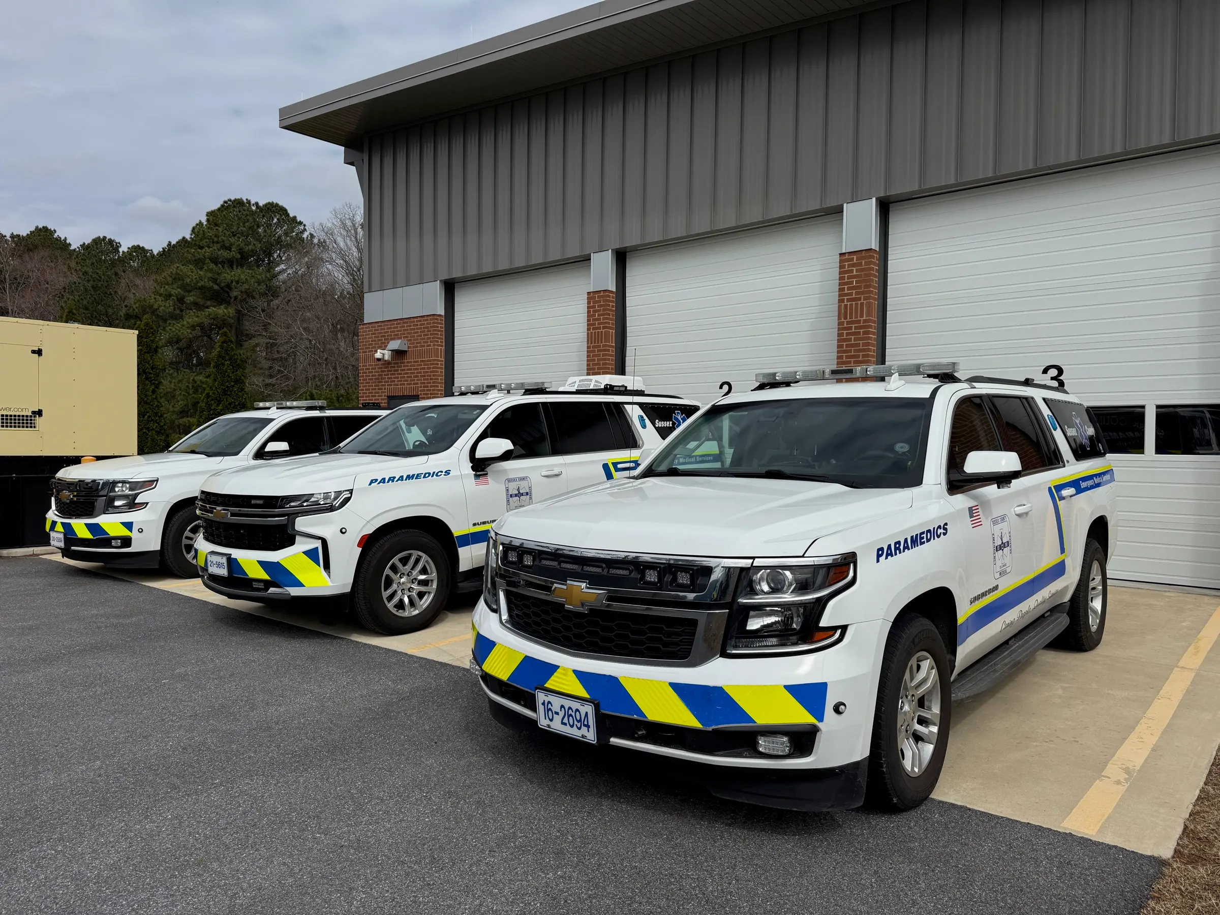 Three paramedic response units parked outside a station's bay doors.
